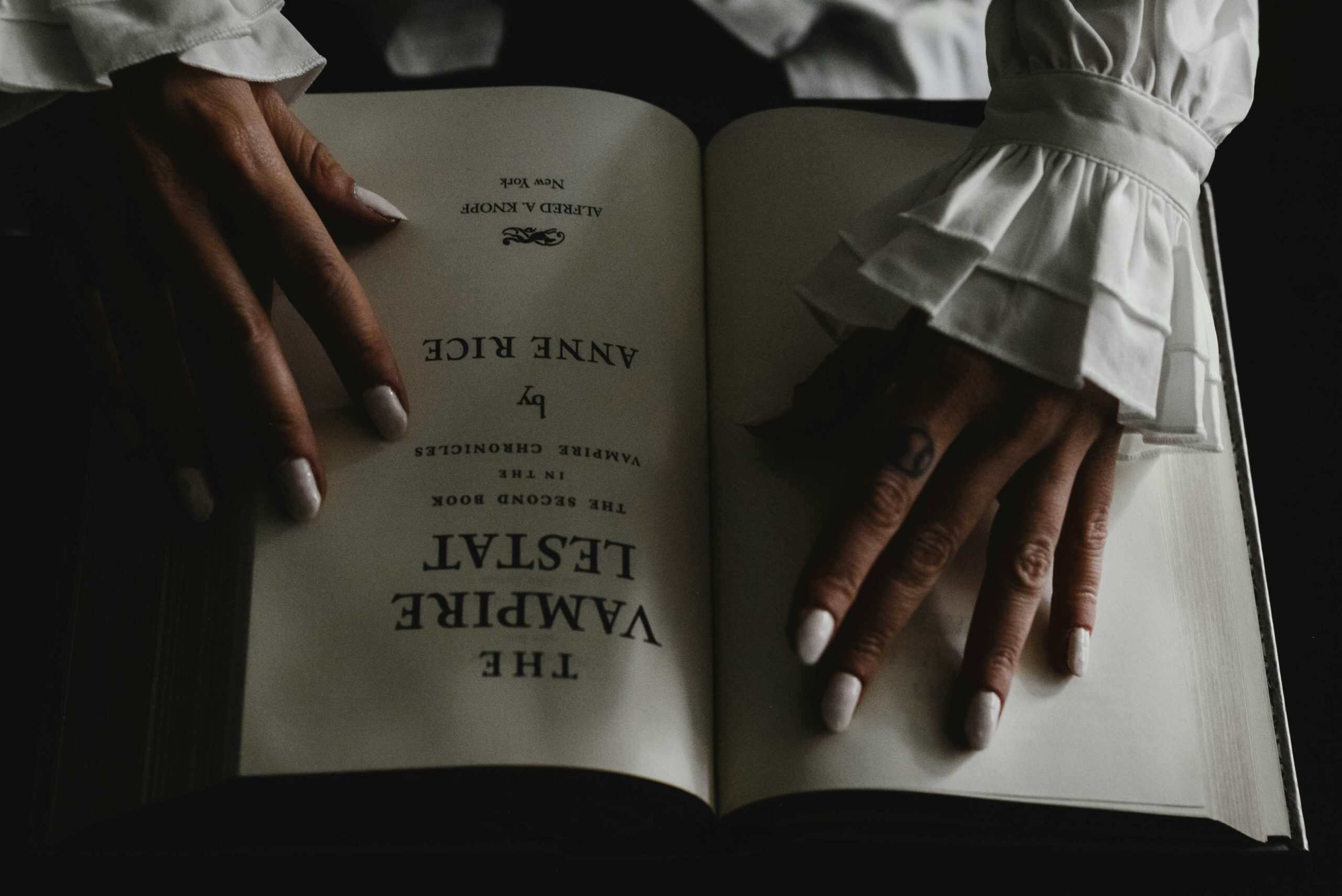 Hands turning pages of a book titled "The Vampire Wane" for villain character development.