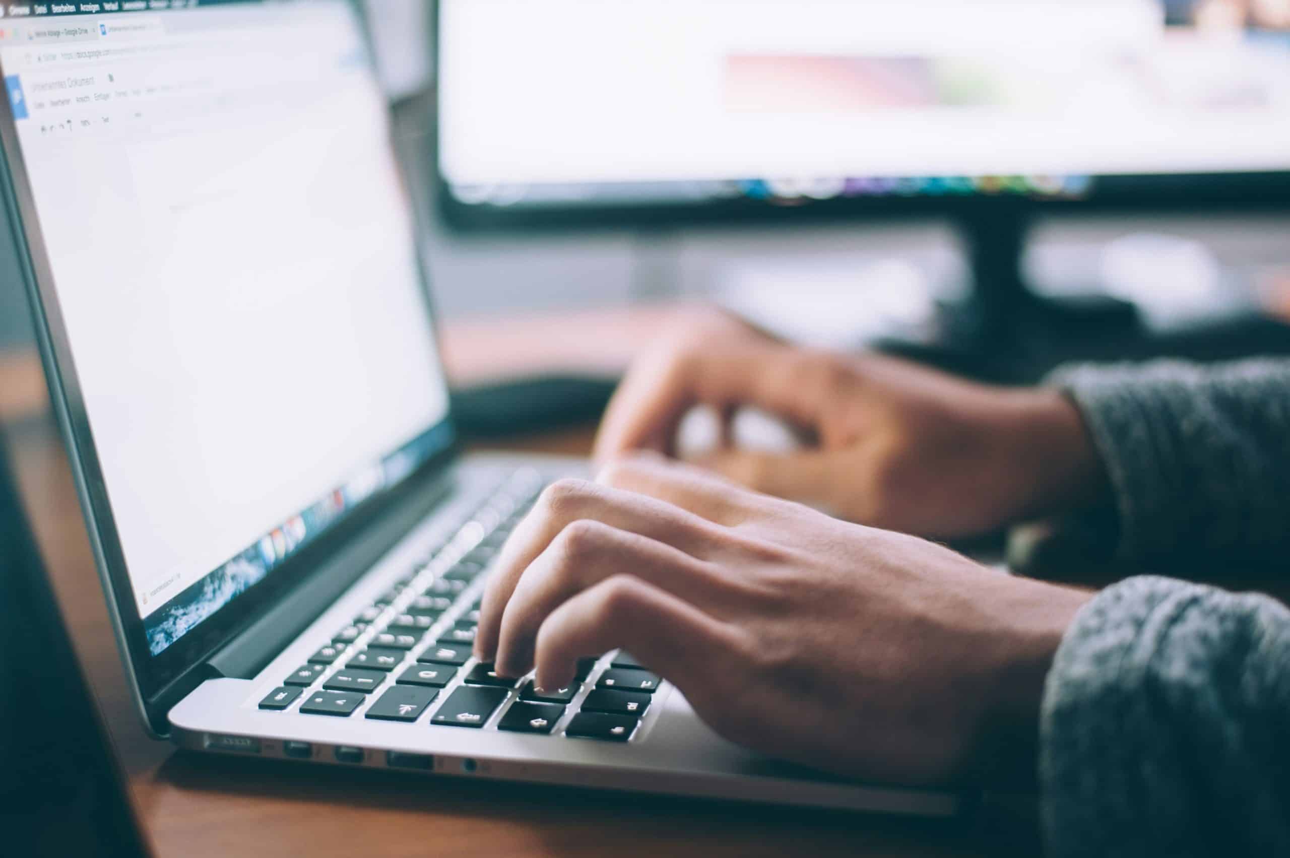 Two hands in frame, typing on a laptop