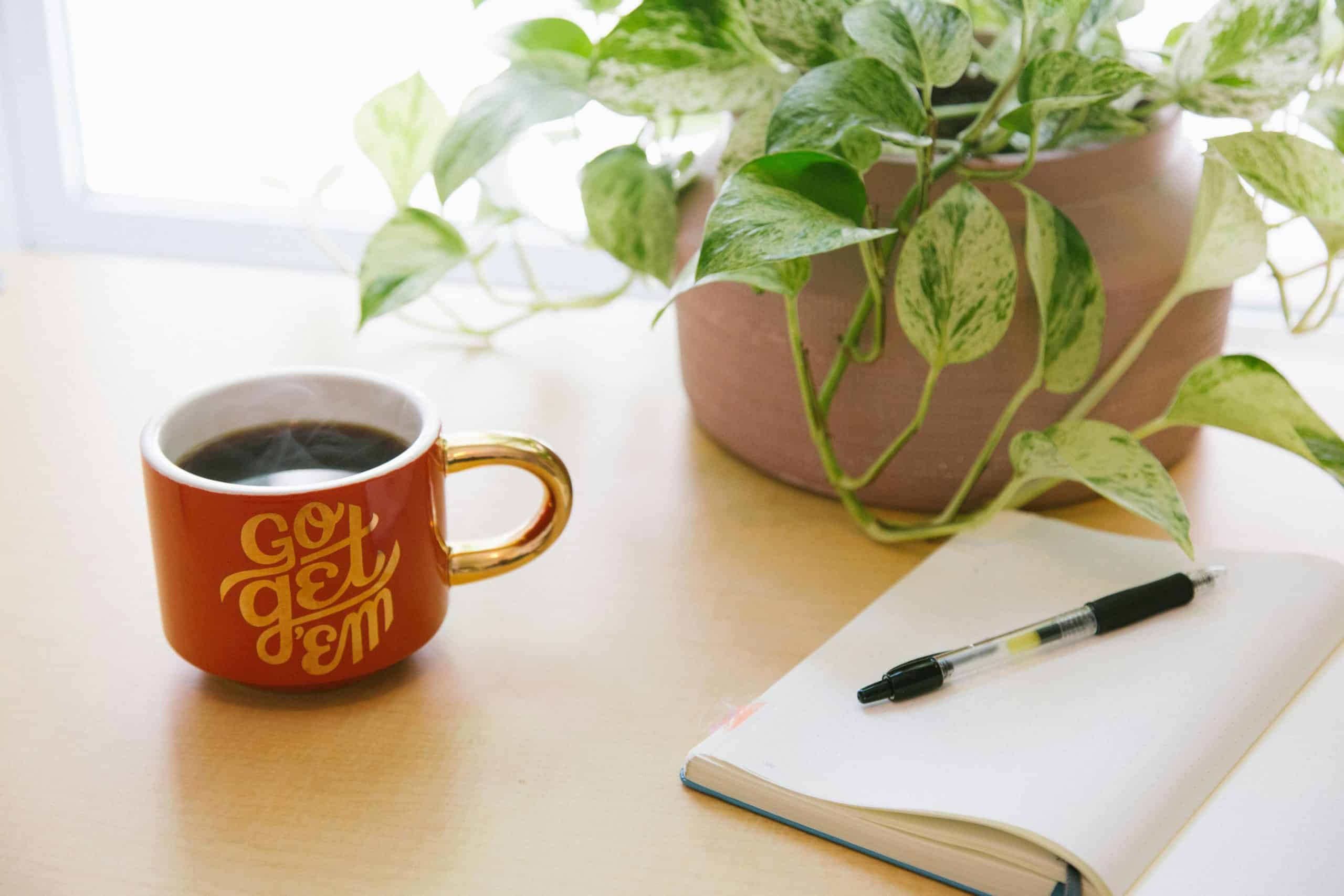 Coffee mug with "Go Get 'Em" motivational message, placed on a wooden desk with a notebook, pen, and.