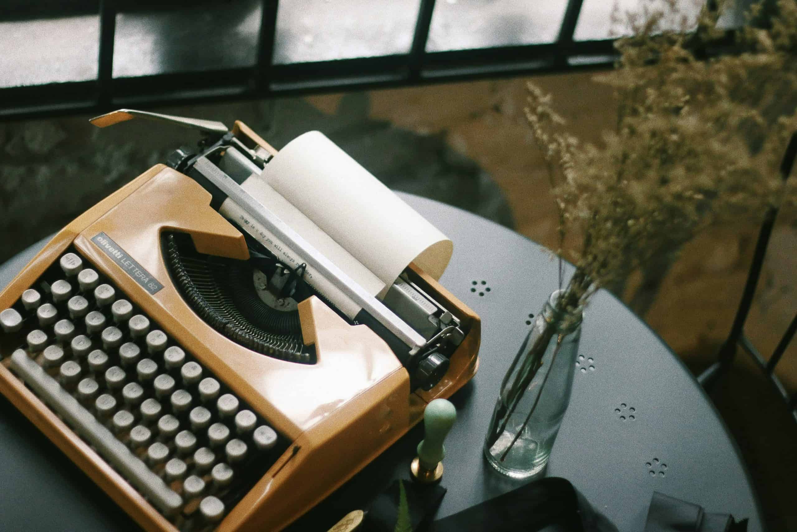 Vintage typewriter on a modern desk with a glass vase and plants. Vintage typewriter on a desk with a glass vase and greenery, perfect for writers and creative spaces.