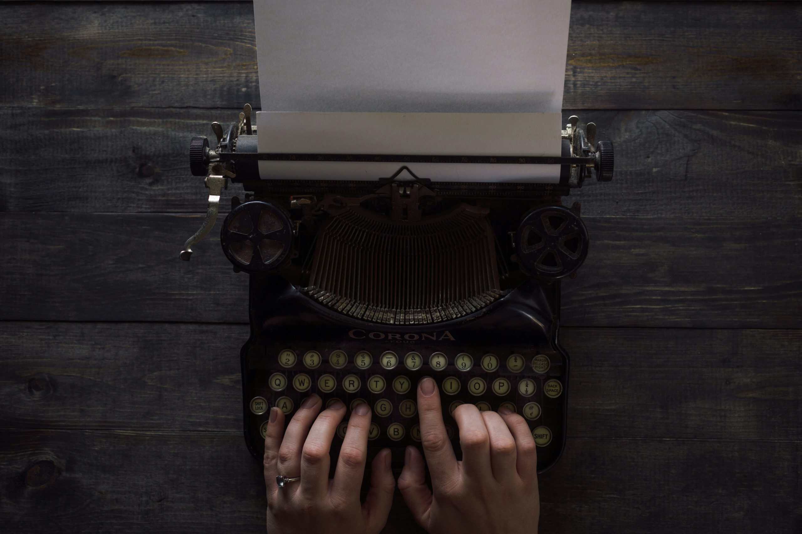 Old-fashioned typewriter on dark wooden surface with hands typing.
