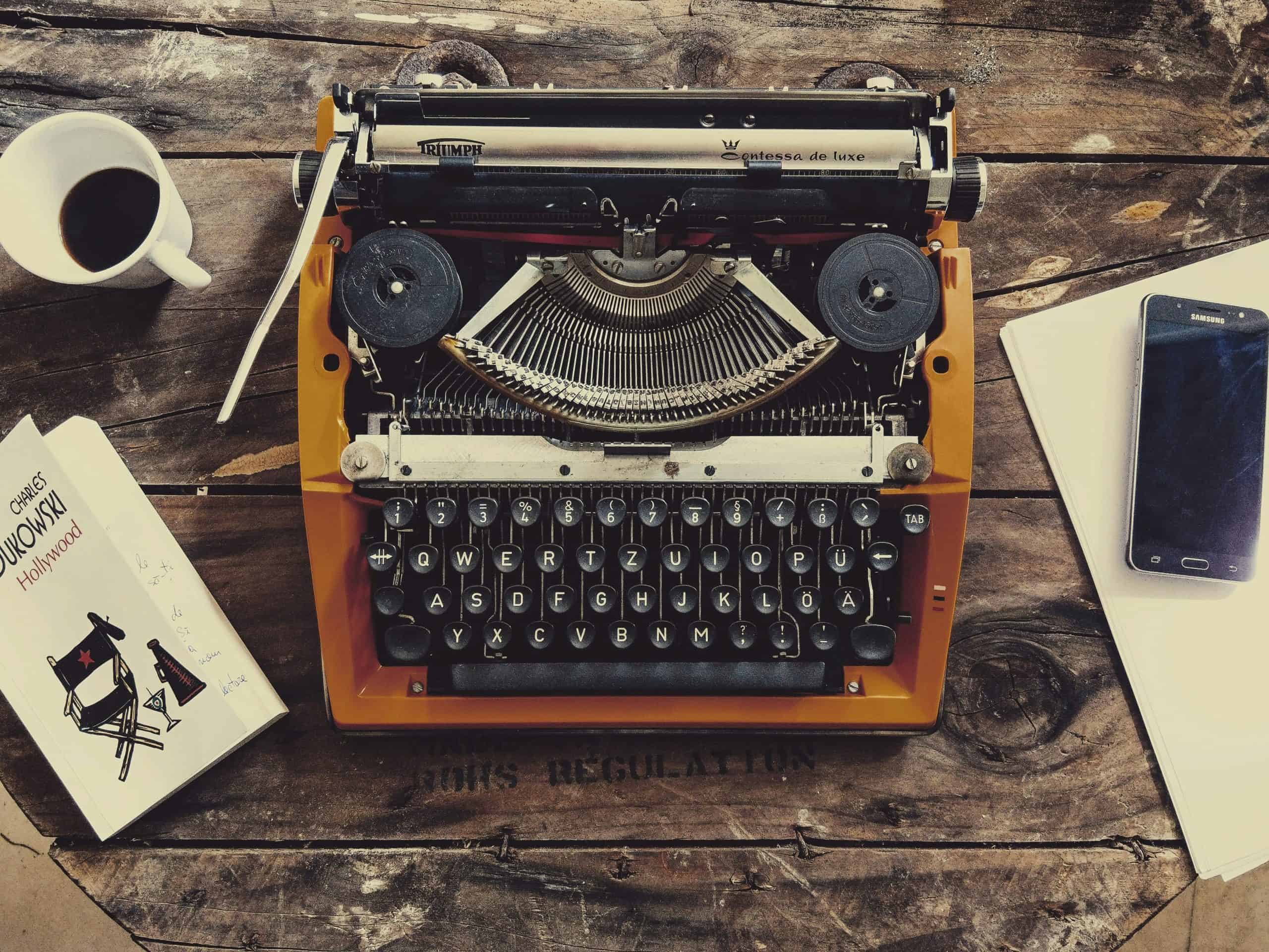 Vintage typewriter on wooden desk with coffee mug, book, and smartphone for writing inspiration.